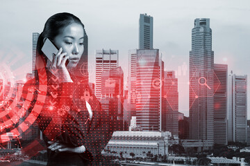 Attractive Asian businesswoman trying to find new ideas using smartphone as a modern tool to solve problems at research and development department. Fintech hologram icons over Singapore.