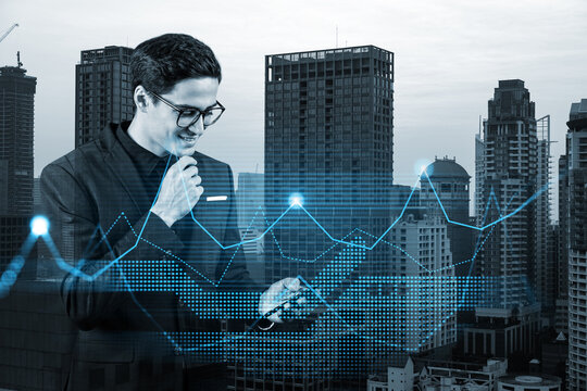 Handsome eastern analyst researches daily analytics using phone to find the financial solution for venture capital project. Hologram chart over Bangkok city background