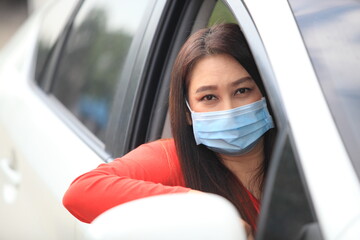  Young woman with medical protective mask on her face is driving a car, she looks into camera and View from outside , Protect yourself.