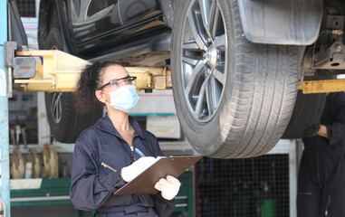 car mechanic on protective mask anti coronavirus and they are fixing car engine in garage