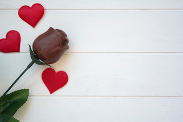 Chocolate rose and red hearts on white wooden table with copy space.