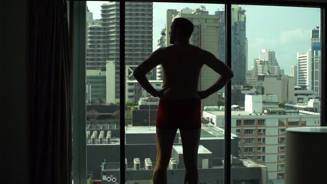 Young man in underwear admire view from window at home, slow motion