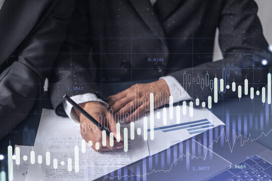 Two traders researching historic data to predict stock market behavior. Women in trading business concept. Forex and financial hologram chart over the table with the document. - Powered by Adobe