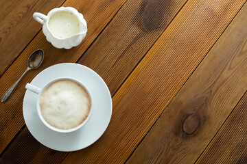Cup of coffee and milk saucer on wooden table with copy space.