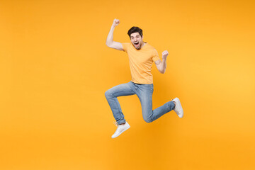 Fototapeta na wymiar Full length of young overjoyed caucasian excited fun man in casual basic t-shirt jeans high jumping up doing winner gesture clenchig fists saying yes isolated on yellow background studio portrait.