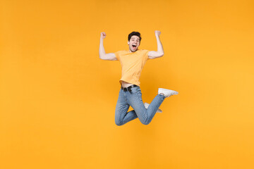 Fototapeta na wymiar Full length of young happy successful overjoyed excited fun surprised man in casual t-shirt jeans high jump up doing winner gesture with clenching fists isolated on yellow background studio portrait.