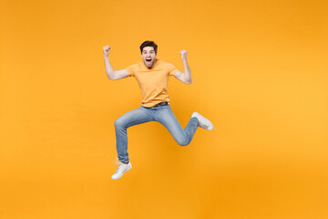 Full length young successful caucasian fun happy surprised man 20s wearing casual t-shirt jeans high jumping up doing winner gesture clenching fists isolated on yellow background studio portrait