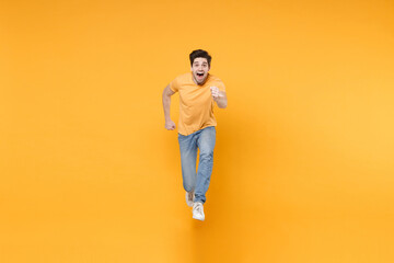 Fototapeta na wymiar Full length young energetic active sporty healthy fast happy surprised man 20s wearing casual basic t-shirt jeans high jumping up running looking camera isolated on yellow background studio portrait.