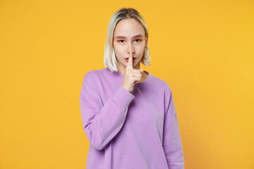 Young blonde caucasian calm woman 20s bob haircut wearing casual basic purple shirt saying hush be quiet with finger on lips shhh secret gesture isolated on yellow color background studio portrait.