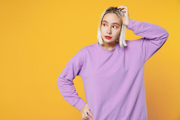 Young blonde caucasian thoughtful pensive confused woman 20s with bob haircut bright makeup wearing basic purple shirt touching head looking aside isolated on yellow color background studio portrait.