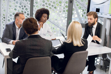 Obraz premium Business, teamwork concept. Group of focused professional international partners, discussing details of joint project in modern meeting room