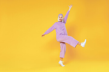 Full length of young blonde caucasian woman 20s bob haircut in casual basic purple suit beanie hat dancing standing on toes spread hands fooling around isolated on yellow background studio portrait