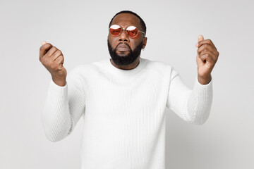 Naklejka premium Displeased upset crying young african american man 20s wearing basic sweater eyeglasses standing spreading hands clenching fists looking camera isolated on white color wall background studio portrait.