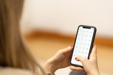 Girl holding smartphone in woman hands, browsing internet or application with blank screen mock-up for your design at home office with blurry background with free space for custom text