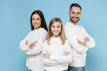 Smiling young parents mom dad with child kid daughter teen girl in white sweaters holding hands crossed isolated on blue color background studio portrait. Family day parenthood childhood concept.