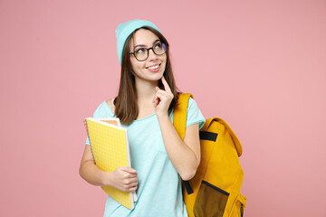 Pensive woman student in blue t-shirt hat eyeglasses backpack hold notebooks put hand prop up on chin isolated on pink background studio portrait. Education in high school university college concept.
