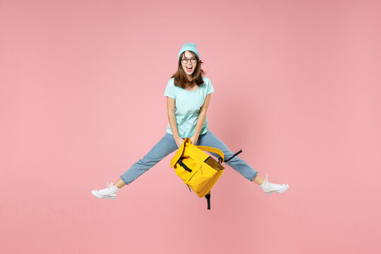 Full Length Portrait Of Excited Young Woman Student In T-shirt Hat Glasses Hold Backpack Jumping Spreading Legs Isolated On Pink Background Studio. Education In High School University College Concept.