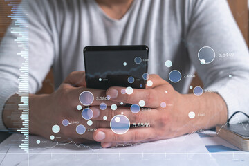 Trader holding in the hands a smart phone and researching stock market to proceed right investment solutions. Internet trading and wealth management concept. Hologram Forex chart over close up shot.