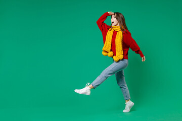 Fototapeta na wymiar Full length side view of excited shocked young brunette woman 20s in knitted red sweater yellow scarf holding hand at forehead looking far away distance isolated on green background studio portrait.