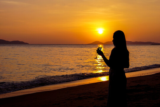 The silhouette of a woman holding a champagne glass on the beach. Blurred picture