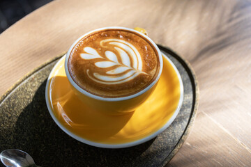 Cup of coffee with latte art on wooden table and morning sunlight with shadow through from window. Beautiful morning.