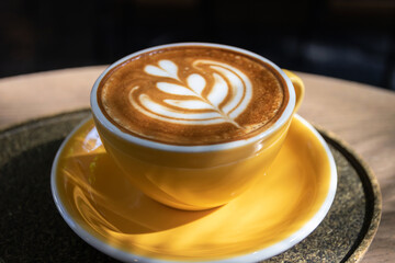 Cup of coffee with latte art on wooden table and morning sunlight with shadow through from window. Beautiful morning.