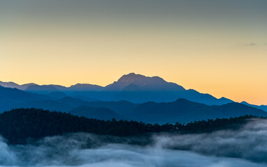 Landscape image of mountain range with fog in sunrise light.