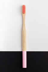 Bamboo toothbrush with pink bristles on a black and white background.