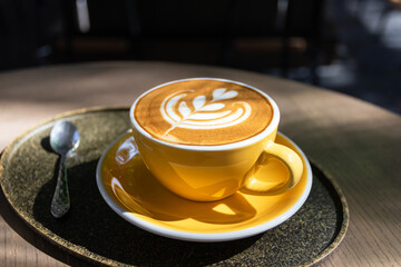 Cup of coffee with latte art on wooden table and morning sunlight with shadow through from window. Beautiful morning.