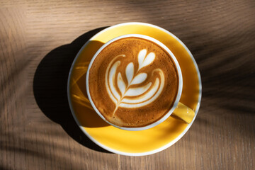 Cup of coffee with latte art on wooden table and morning sunlight with shadow through from window. Beautiful morning.