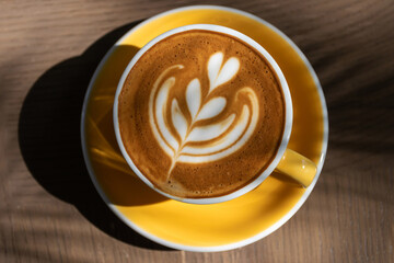 Cup of coffee with latte art on wooden table and morning sunlight with shadow through from window. Beautiful morning.