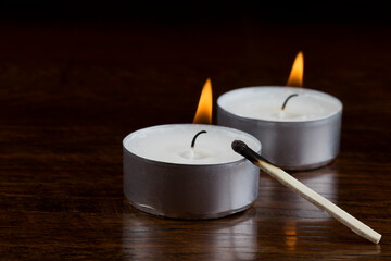 burning tealight candle pair in the dark with matchstick - obrazy, fototapety, plakaty