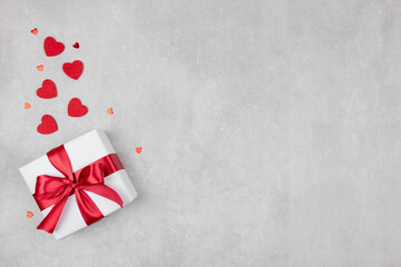 Valentines Day background with gift and red hearts confetti on light concrete background....