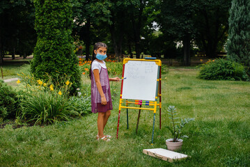 A school girl in a mask stands and writes lessons on the blackboard. Back to school, learning during the pandemic