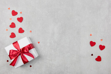 Valentines Day background with gift and red hearts confetti on light concrete background. Valentines or mothers day, birthday, holiday concept. Flat lay, top view, copy space.