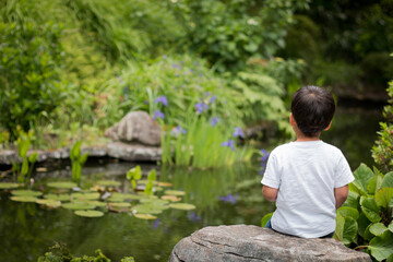 Thoughtful boy sitting by a pond in a calm, peaceful setting at Tupare Gardens in New Plymouth, North Island, New Zealand