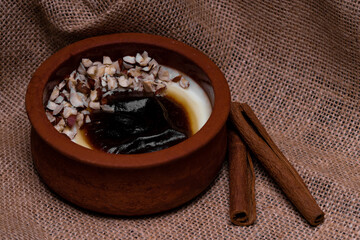 Turkish traditional dessert in earthenware casserole with cinnamon sticks and hazelnut; sutlac. Baked Rice Pudding. Horizontal close-up macro shot. High resolution sharp photo.