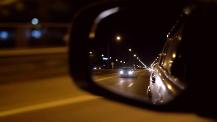 mirror of car driving on a night city road with a car following 