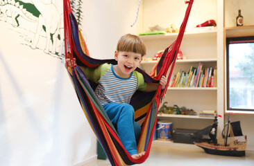 Ein vierjähriger Junge sitzt in einer Hängeschaukel in seinem Kinderzimmer