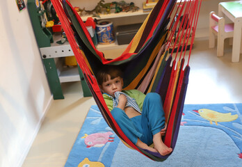 Ein vierjähriger Junge sitzt in einer Hängeschaukel in seinem Kinderzimmer