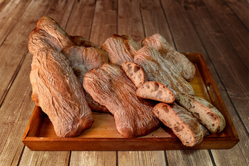 Italian ciabatta bread, many whole loaves and cut loaves in half in wooden tray on rustic wooden...