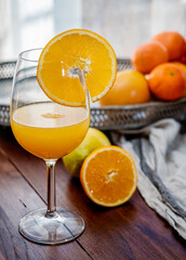 Crystal glass with orange juice, citrus background and cut orange. Colors yellow and orange.