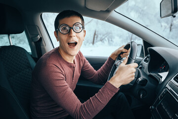 Funny and ridiculous idiotic nerd driver in big eyeglasses holding the steering wheel and smiling...