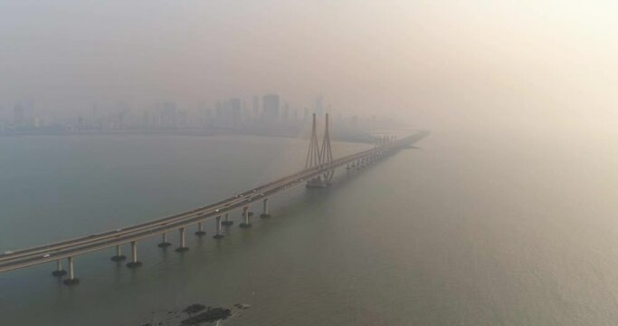 A drone shot at Bandra Worli Sea Link seen from an aerial view in slow motion. Cinematic drone movement with the iconic Mumbai Sea Link at the forefront and the city view in the background.