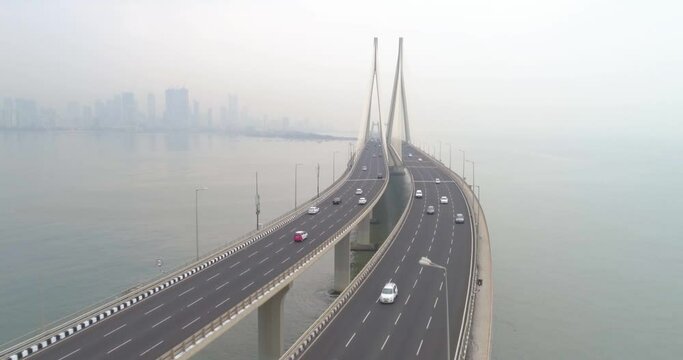 A drone shot at Bandra Worli Sea Link seen from an aerial view in slow motion. Cinematic drone movement with the iconic Mumbai Sea Link at the forefront and the city view in the background.
