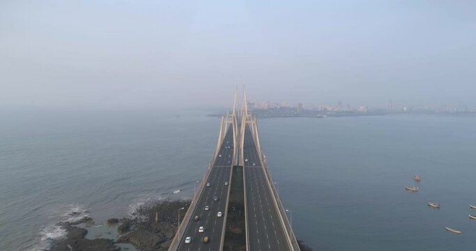 A drone shot at Bandra Worli Sea Link seen from an aerial view in slow motion. Cinematic drone movement with the iconic Mumbai Sea Link at the forefront and the city view in the background.