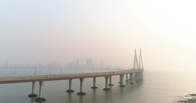A drone shot at Bandra Worli Sea Link seen from an aerial view in slow motion. Cinematic drone movement with the iconic Mumbai Sea Link at the forefront and the city view in the background.