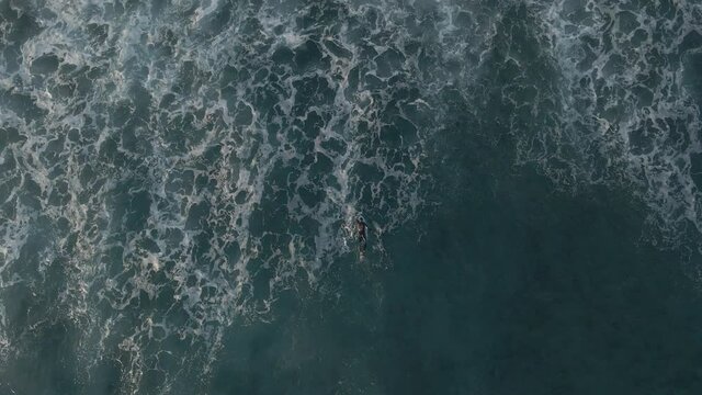 Lonely surfer paddling in the ocean aerial top view