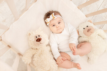 Fototapeta premium the baby is six months old in a crib in a white bodysuit with a Teddy bear