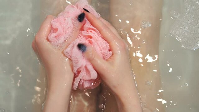 Woman holding pink sponge and soaping it using shower gel.